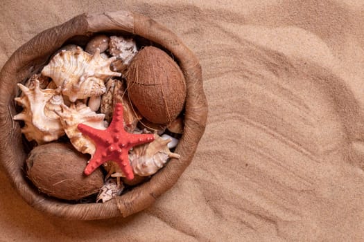 Seashells in a wicker basket on the sand. Summer holidays at sea background with space for text. View from above.