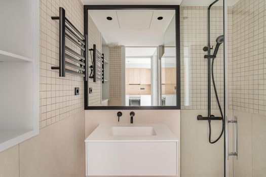 Modern interior design of bathroom in beige with black metal decoration. Front view of mirror and sink in refurbished apartment
