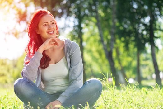 Portrait of a young attractive woman. Sitting cross-legged in the park