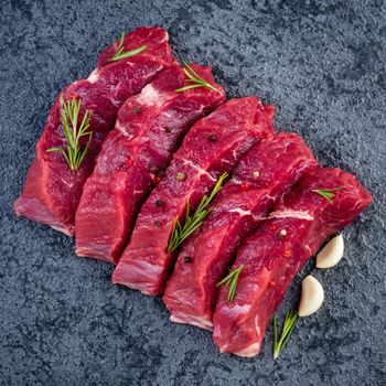 Raw meat, beef steak with seasoning on a black stone table, top view