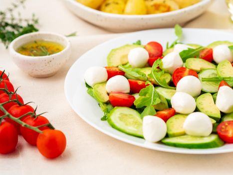 Fresh salad with tomatoes cucumbers arugula mozzarella and avocado. Oil with spices rosemary, thyme, side view