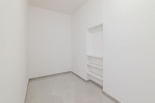Empty small room with white walls and built-in niche for shelves in an old flat before renovation