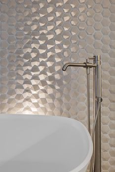 Metal faucet and shower in bathroom with hexagon tiles and white bath tub.