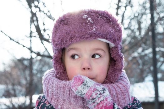 Winter, games, family, childhood concepts - close-up portrait authentic little preschool minor 3-4 years girl in pink hat look at camera posing smiles in snowy frosty weather. Funny kid eat taste snow.