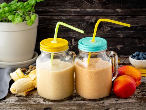 banana peach nectarine smoothie in two jars, fresh fruit milkshakes on the old dark rustic wooden table, side view