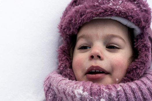 Winter, family, childhood concepts - close-up portrait authentic little preschool girl in pink clothes smile laugh shout with open mouth laying on snow in frosty weather day outdoors. Funny kid face.