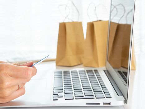 woman sitting at table, looking at laptop, pay for purchases by credit card, online shopping.