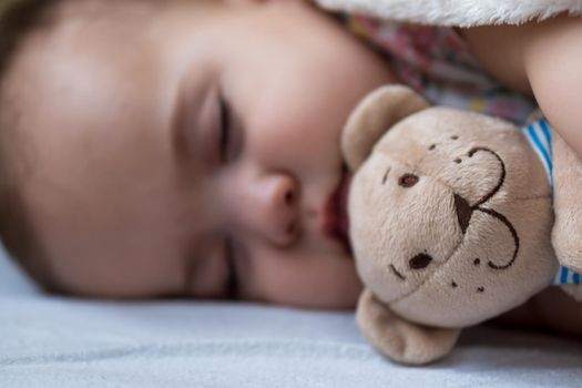 Childhood, care, motherhood, health concepts - Close up Little peace calm infant toddler baby girl sleep resting take deep nap laying hug teddy bear toy on soft warm blanket with close eyes on big bed.