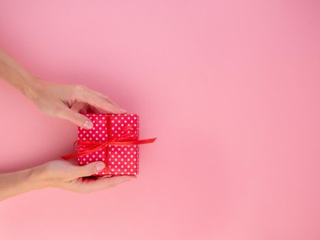 woman holding a gift in a red gift box with a bow, pink background, top view, empty space for text.