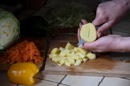 a woman cuts potatoes in the kitchen against the background of fresh vegetables, ingredients for step by step cooking soup. High quality photo