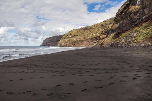 Empty wild beach with foot steps on black sand. Rocks and ocean on Tenerife, Canary Islands, Spain
