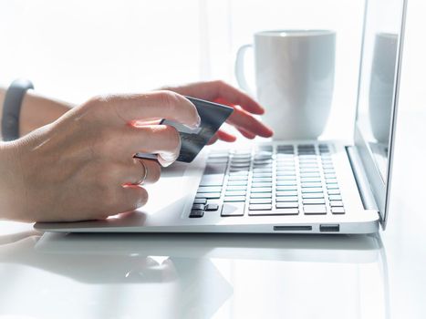 woman sitting at a table, drinking tea and looking at a laptop, pay for purchases by credit card, online shopping.