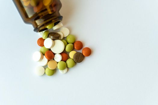 Medicine and pills. Multi-colored medicines on a white background close-up. Brown glass bottle with pills inside on a white background. Multi-colored tablets that spilled from an inverted jar onto a white surface