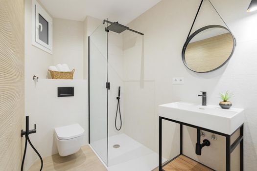 Modern style bathroom in bright colors in refurbished apartment. Shower zone, sink with black faucet and round mirror frame