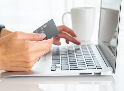woman sitting at a table, drinking tea and looking at a laptop, pay for purchases by credit card, online shopping.
