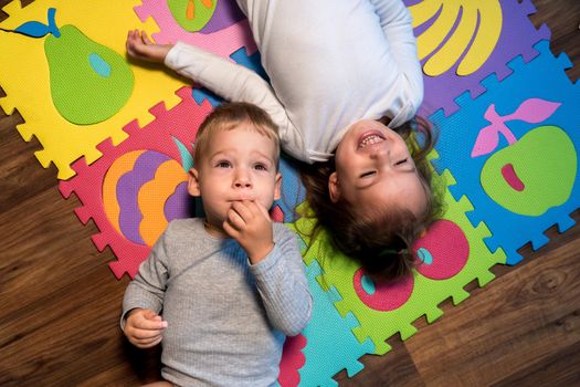 childhood, family friendship, games - close up portrait Two funny joy happy smiling little toddler peschool kids siblings twins brother with sister have fun lie playing on puzzles mat at home indoors.