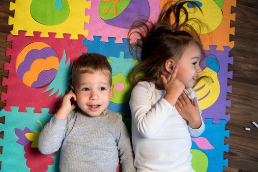 childhood, family friendship, games - close up portrait Two funny joy happy smiling little toddler peschool kids siblings twins brother with sister have fun lie playing on puzzles mat at home indoors.