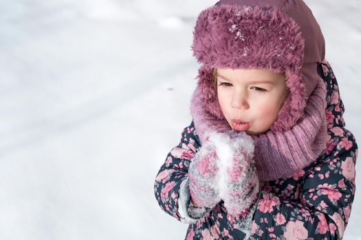 Winter, games, family, childhood concepts - close-up portrait authentic little preschool minor 3-4 years girl in pink hat warm clothes have fun smiles in snowy frosty weather. Funny kid eat taste snow.