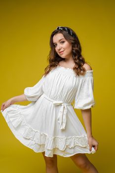 Beautiful bright woman in the studio on a yellow background in a white light dress smiling happy,