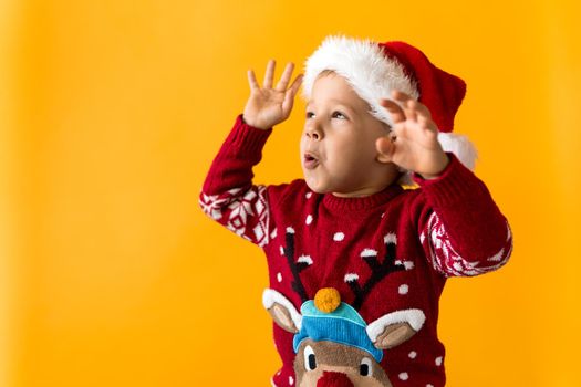 Portrait of happy smiling positive joyful positive preschool little boy in red warm santa hat showing thumb up on orange, yellow background. Winter, holiday, celebration, Christmas, New Year copy space.