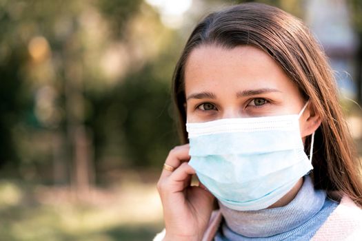 care, infants, spring, coronavirus and quarantine concept - Young cute long haired woman European Caucasian Slavic appearance put on blue medical protective mask in midday sunlight backlight in park