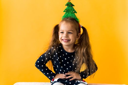 Portrait of positive smiling surprised happy little schoolgirl girl Christmas tree decoration on head polka dot dress show thumbs up orange background. New year, holiday, celebration, winter concept.