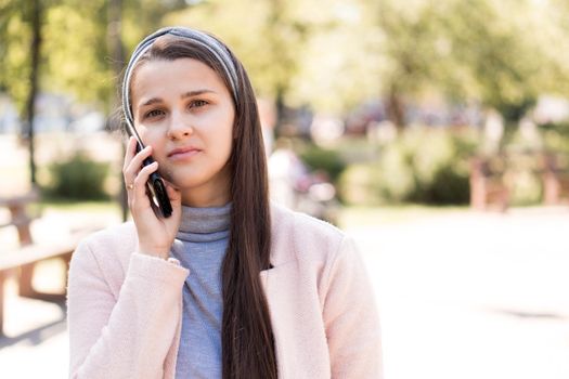care, spring, cvid-19, quarantine concept - Young happy nice cute long haired smiling woman European Caucasian Slavic appearance in pink and grey talking on phone in midday sunlight backlight in park.