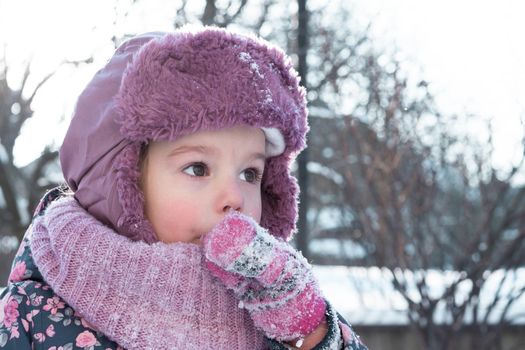 Winter, games, family, childhood concepts - close-up portrait authentic little preschool minor 3-4 years girl in pink hat look at camera posing smiles in snowy frosty weather. Funny kid eat taste snow.