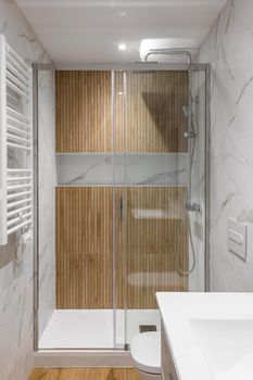 Shower zone with wooden finishing and glass door. Interior of modern refurbished bathroom.
