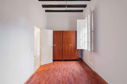 White room interior with wooden wardrobe, black beams, window and boot marks on the parquet.