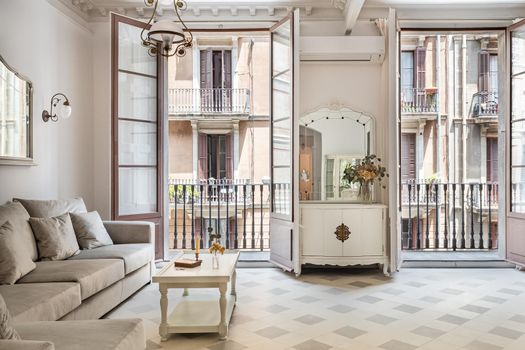 Front view to the vintage style living room with sofa, tile floor, retro lamps and balconies. Refurbished apartment in Barcelona old city