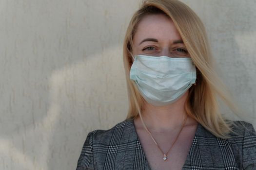 Close-up portrait of a young blonde woman in a medical mask on a light background. Virus protection. Coronovirus covid-19 The concept of a pandemic epidemic. Quarantine. Stay at home