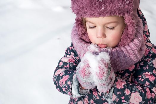 Winter, games, family, childhood concepts - close-up portrait authentic little preschool minor girl in pink hat warm clothes have fun smiles in cold frosty weather day. Funny kid blow on white snow.
