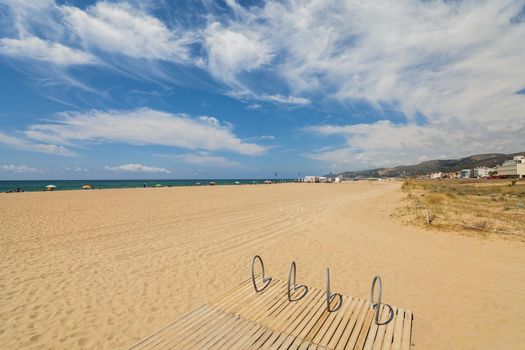 Castelldefels beach with sand dunes and stand for bicycles. Sunny day with blue sky.