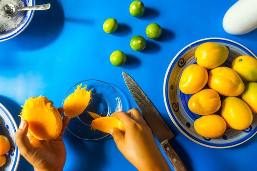 top view of the hand of a latin woman peeling mangoes on a glass plate and with traditional summer fruits in nicaragua, central america and latin america