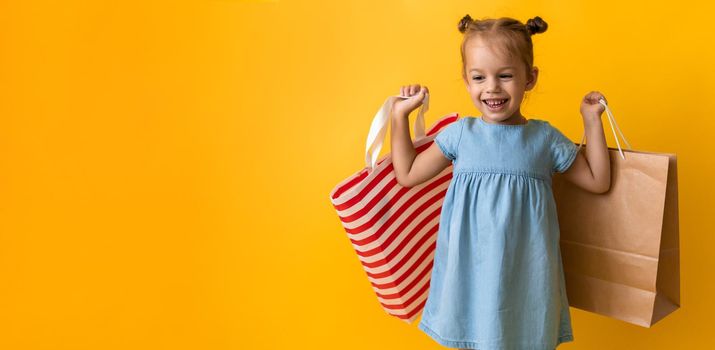 Banner Portrait Caucasian Beautiful Happy Little Preschool Girl Smiling Cheerful And Holding Cardboard Bags Isolated On Orange Yellow Background. Happiness, Consumerism, Sale People shopping Concept.