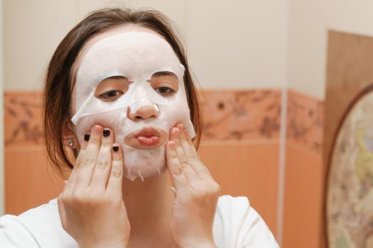 A cheerful and funny girl fooling around and grimacing in a moisturizing face mask. Morning beauty treatments, oily and combination skin care concept