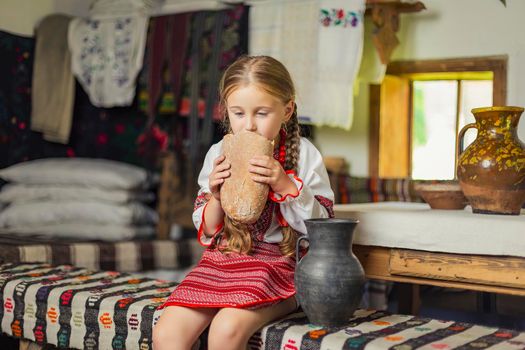 girl in Ukrainian national costume eats bread sitting on a bench in the house