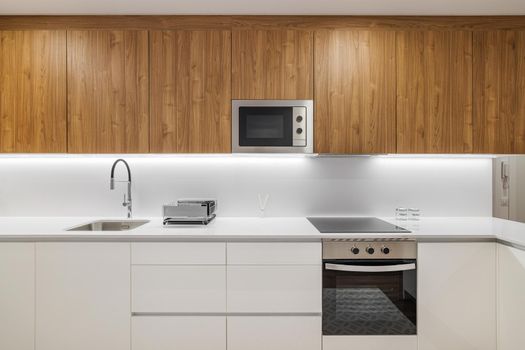 Stylish kitchen with modern furniture in white color with wooden cupboards for kitchenware. Contemporary style interior after home renovation.