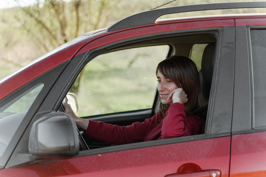 Dark-haired smiling girl in a burgundy sweatshirt driving a teracotta car