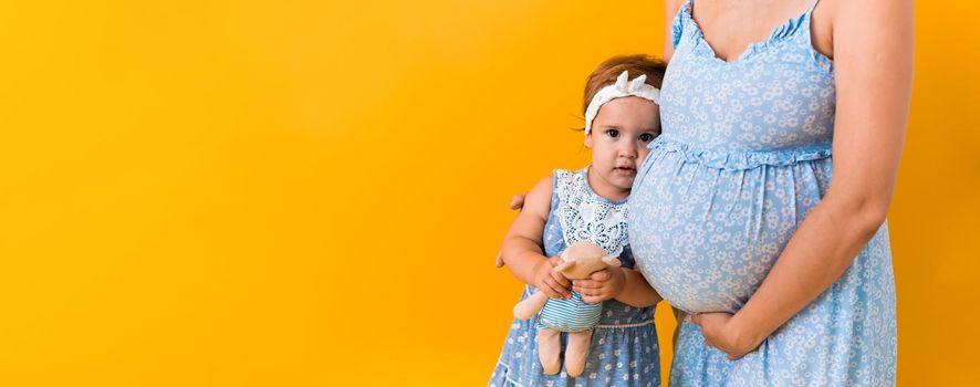 Motherhood, femininity, hot summer - croped banner pregnant unrecognizable woman mother in blue dress little happy girl baby sibling with teddy bear hugs care mom's big belly on yellow background.