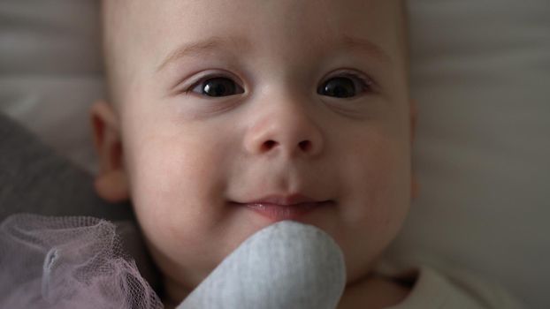 Close-up Happy playful kid 6 month old. Newborn boy looking at camera after bath shower on white soft bed. baby child waking time before bedtime with Toy. Childhood, motherhood, family, infant concept.