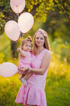 mother with daughter in her arms and balloons in identical dresses