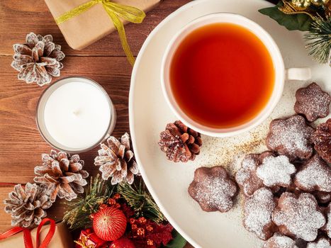 Christmas or new year card. Winter holiday composition, side view, flat lay, brown wooden background. Tea, cookies, fir cones, candles, gift