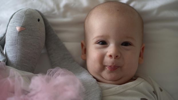 Close-up Happy playful kid 6 month old. Newborn boy looking at camera after bath shower on white soft bed. baby child waking time before bedtime with Toy. Childhood, motherhood, family, infant concept.