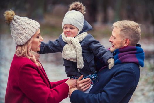 young family with a baby in their arms are walking in the park in winter