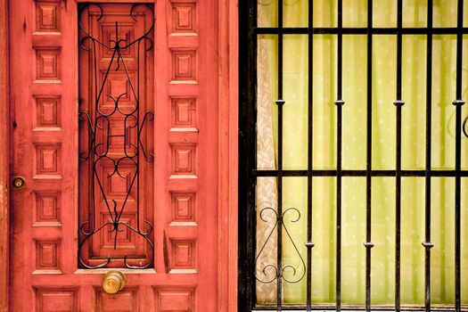 Wooden door next to window with gree curtain and forged metal grill