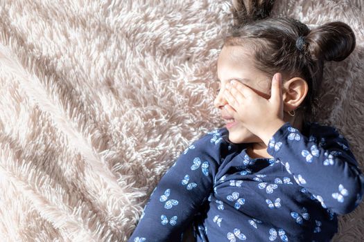 Middle Eastern young cute girl lies on a light bed in the light of sunlight. Persian swarthy girl on the bed. Middle Eastern kids on the bed