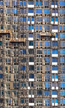 The facade of a high-rise residential building under construction at the stage of its insulation with mineral insulation. The windows reflect the blue sky, a vertical image.