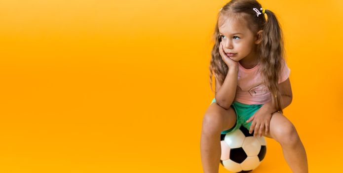 Authentic cute smiling preschool little girl with classic black and white soccer ball look at camera on yellow background. child play football in t-shirt and shorts. Sport, championship, team concept.